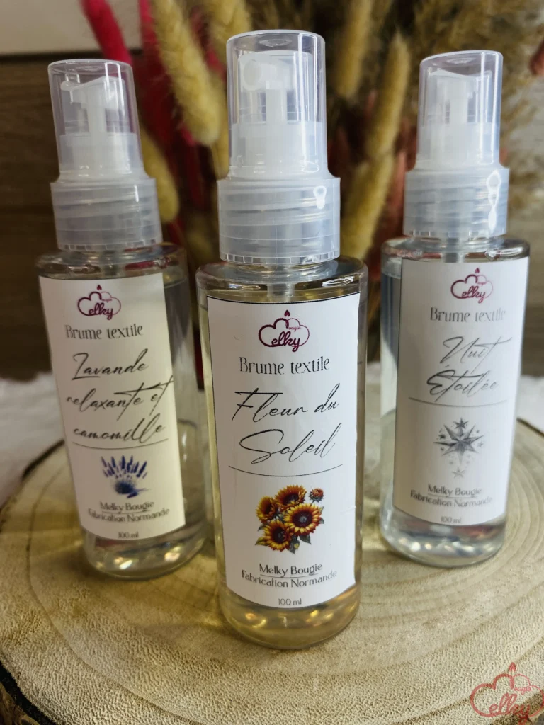 Trois flacons de brume textile Melky Bougie posés sur un support en bois. Chaque flacon porte une étiquette élégante indiquant son parfum : "Lavande relaxante et camomille", "Fleur du Soleil" et "Nuit étoilée". En arrière-plan, un bouquet de fleurs séchées aux teintes naturelles et rosées ajoute une touche décorative et chaleureuse.